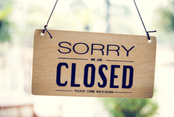 Wooden hanging sign saying 'Sorry, we are closed' with 'please come back again' text on a glass window/door.