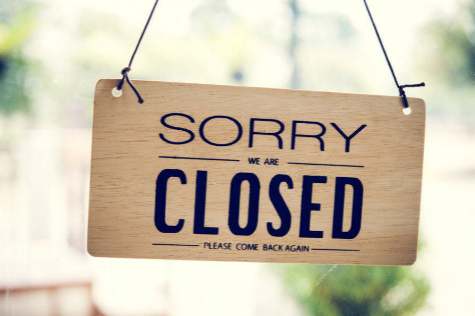 Wooden hanging sign saying 'Sorry, we are closed' with 'please come back again' text on a glass window/door.
